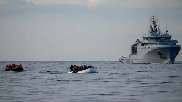 Two inflatable dinghies carrying migrants pass a French navy vessel in the English Channel