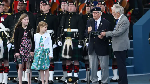 Eric Bateman reads speech in front of soldiers in uniform, while grandchildren look on