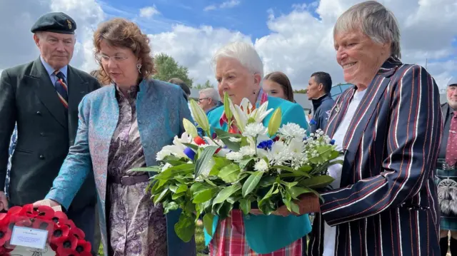 Three women laying wreaths and flowers at the memorial site at Pegasus Bridge