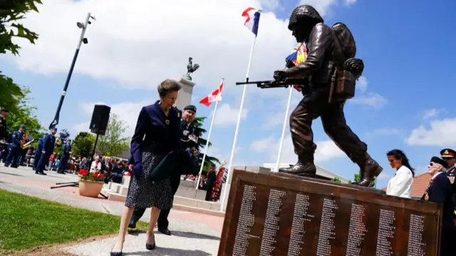 Princess Anne looking at statue of soldier with lines of names written on its base