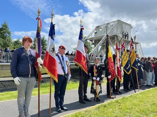 Volunteers holding flags and colours of the various forces involved in the capture of Pegasus Bridge