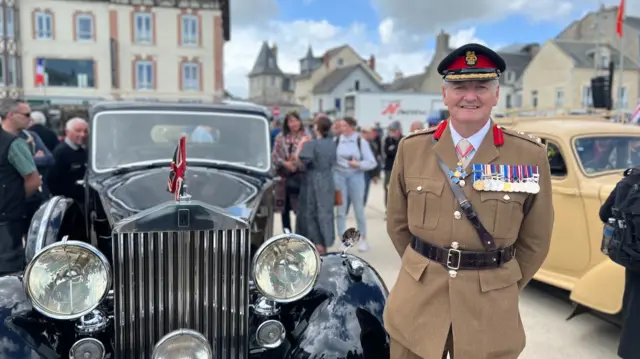 Brigadier Mike Caldicott CBE in army uniform, smiling, and standing next to black classic car