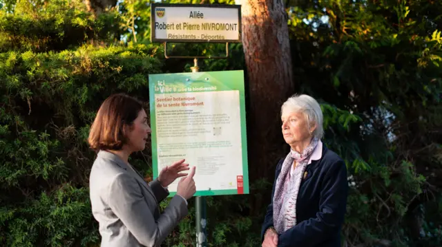 Katya Adler stands with Catherine Nivromont next to a street sign "Allee Robert et Pierre Nivromont"