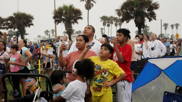 People hold up their phones as they watch SpaceX's Starship rocket launch