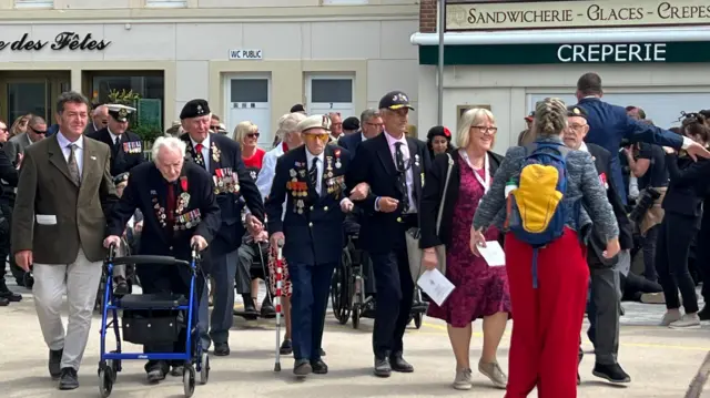 D-Day veterans walking across a square wearing suits and medals