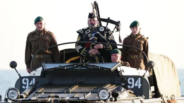 A military piper comes into shore on a DUKW amphibious vehicle ahead of playing a dawn lament on Gold Beach in Arromanches in Normandy, France