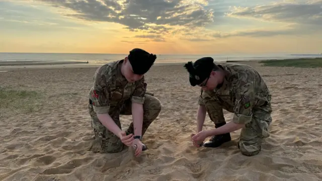 Two army cadets gather sand on a French beach