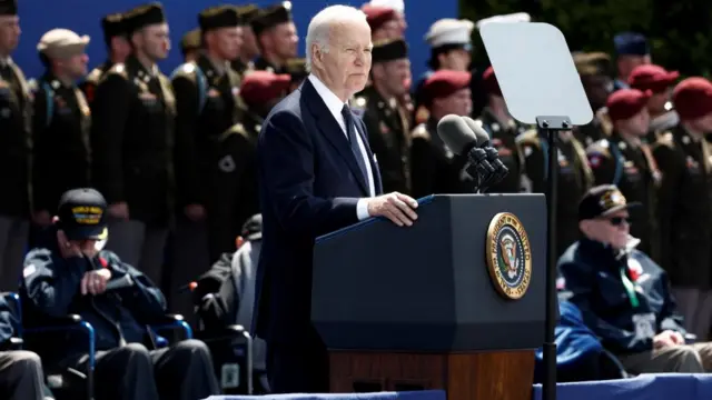Biden speaks at a lectern, as veterans stand and sit behind him
