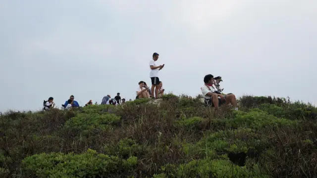People sit on a hillside and wait for SpaceX's Starship rocket launch
