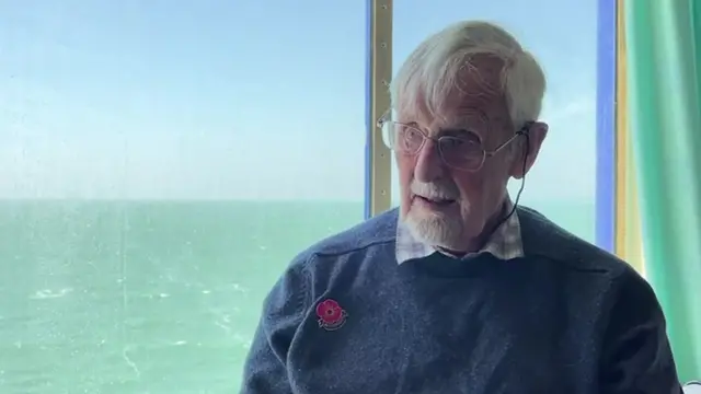 Jack Hemmings speaks to the BBC. The sea can be seen through a boat window behind him