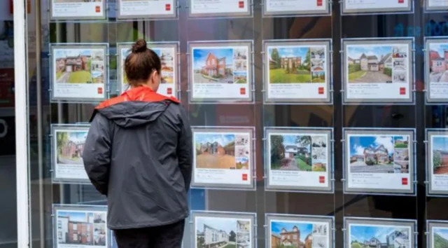 A woman looks at an estate agents houses on offer in the window