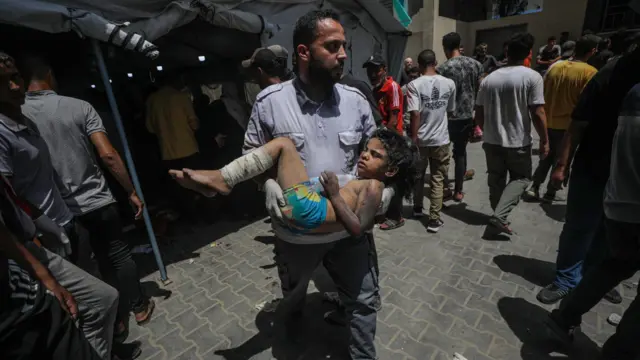 A Palestinian medic carries a wounded child following an Israeli military operation in al-Nuseirat refugee camp