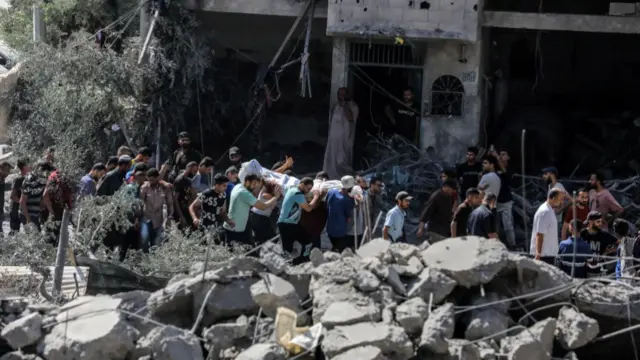 Palestinians carry a body wrapped in a white shroud through the rubble following Israel's strikes in Gaza