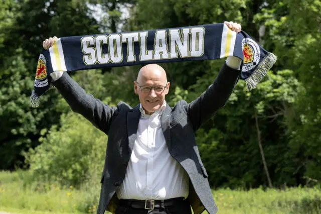 John Swinney holds up a Scotland scarf