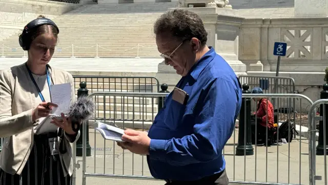 A man in a blue shirt stands in front of the Supreme Court