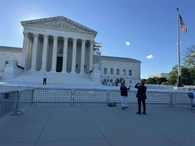 Court building with security guard, woman in white pants and dark top, man in dark suit with phone