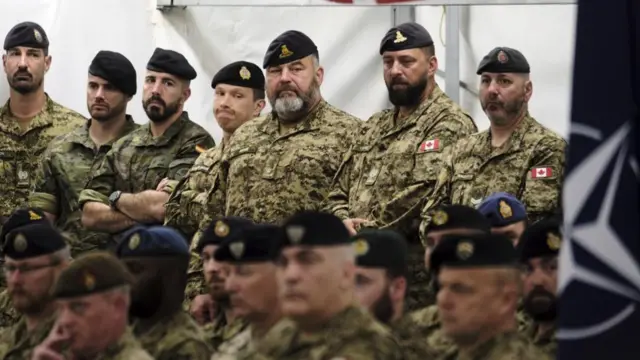 Nato soldiers sit and stand in a group as they listen to a speech during a ceremony in Latvia last week