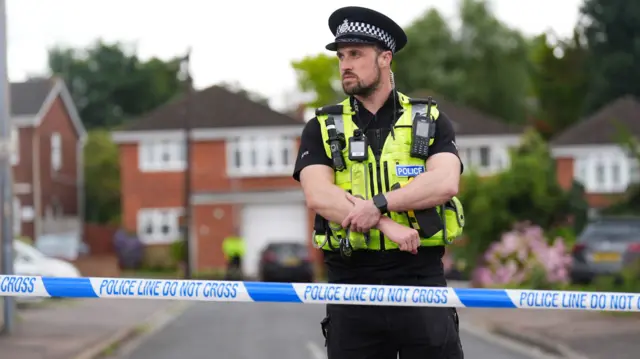 Police officer stands in front of blue police tape cordoning off a residential street