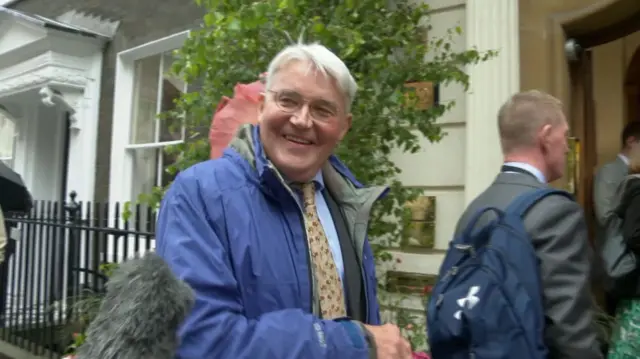 Andrew Mitchell being doorstepped, wearing a raincoat