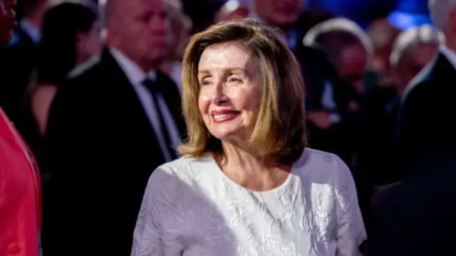 Nancy Pelosi wearing white dress, smiling