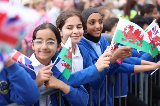 A group of schoolchildren line the barrier holding Welsh flags