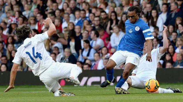 John Bishop and Ben Shephard of England tackle Edgar Davids during Soccer Aid 2014 at Old Trafford