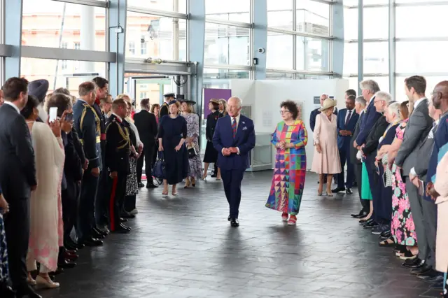 King Charles walks down the entrance of the Senedd building while two lines of people watch him