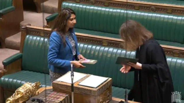 Suella Braverman stands in front of the Commons staffer, holding a text