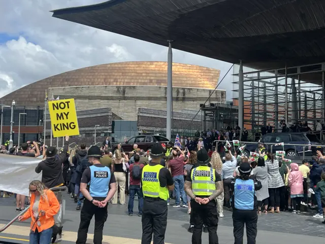 Protestors outside the Senedd building behind a crowd of people as the King greets them