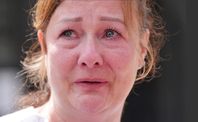 A headshot of Lea Holloway with tears in her eyes. She has mid-brown hair which is tied up