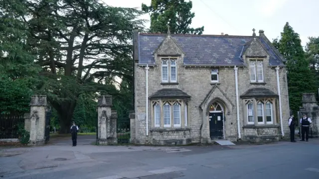 Stone gateposts at entry to cemetery. Police officer stands guard between the posts.