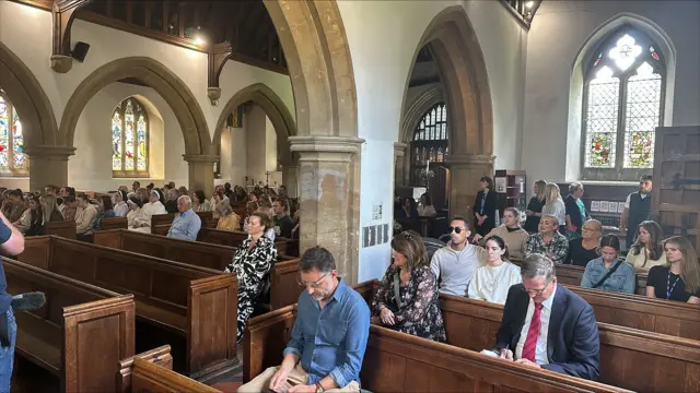 People sitting in pews, some with their heads bowed, inside St James's church in Bushey