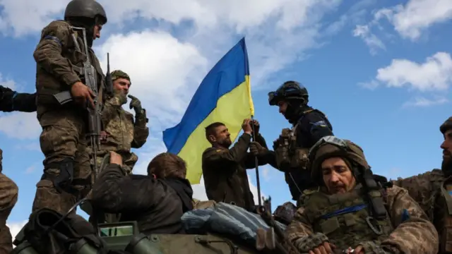 Ukrainian soldiers adjust a national flag atop a personnel armoured carrier on a road near Lyman, Donetsk region, on 4 October 4 2022