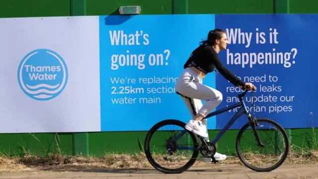 A woman riding a bike past a Thames Water sign