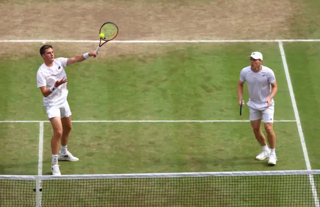 Henry Patten hits the balls with his tennis racquet while he stands next to partner Harri Heliovaara