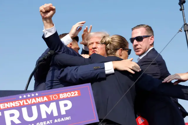 Trump raises a fist in the air while surrounded by Secret Service agents