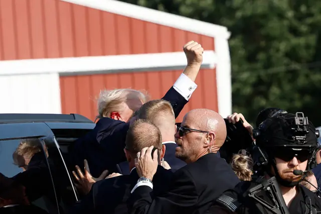 Trump pumps his fist as he is rushed into a car