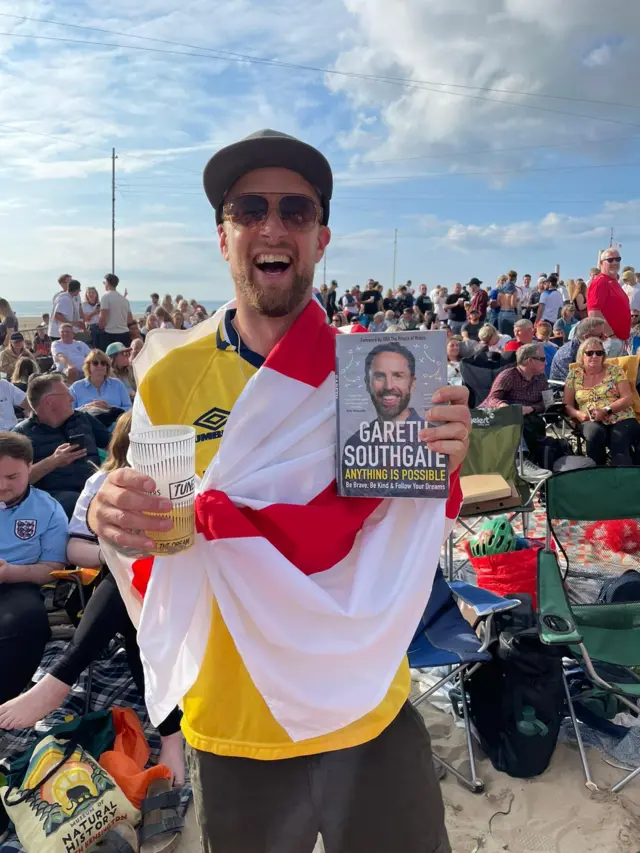 Fan holds Southgate's book while draped in an England flag