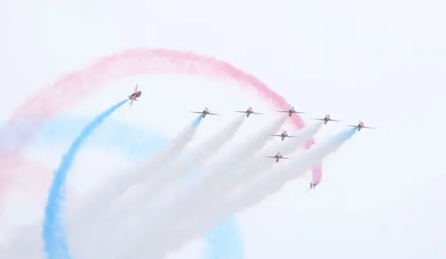 Red Arrows team stream white trails, surrounded by red and blue