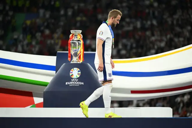 Kane walks past the trophy with his runners up medal