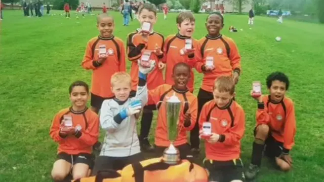 the young Cray Wanderers team celebrate winning a trophy with Marc Guehi on his knees at the front holding the trophy