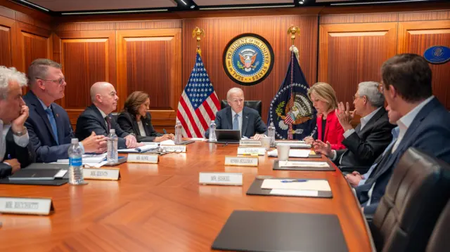 President Biden sits in a wood-panelled situation room, surrounded by advisors