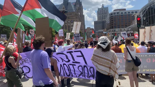 Protesters stand with banners and Palestine flags in the street