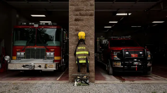 Comperatore's fireman's jacket is displayed in front of two fire-fighting vehicles