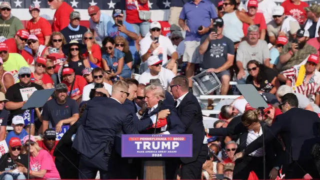 Former President Donald Trump is assisted by US Secret Service personnel after he was shot in the right ear during a campaign rally