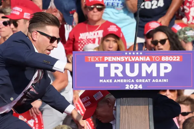 Former US President Donald Trump and security personnel react as multiple shots rang out during a campaign rally at the Butler Farm Show in Butler, Pennsylvania