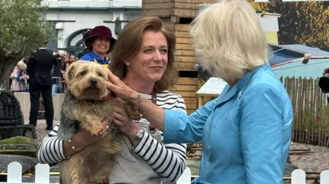 Queen Camilla stroking a dog being held by a woman