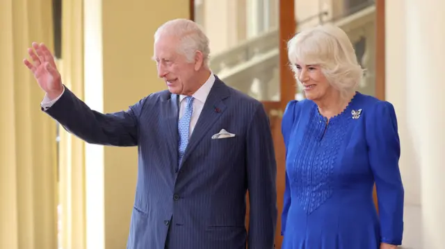 King Charles and Queen Camilla smile and wave