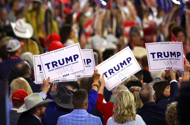 People in a crowd hold up placards that have Trump printed on them, with Vance written in black pen underneath