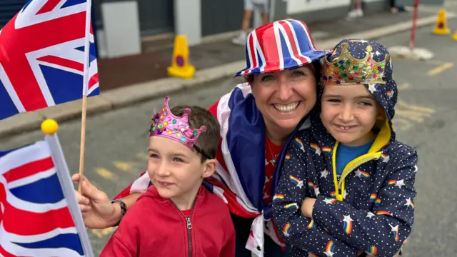 Two boys stood with mother carrying flags